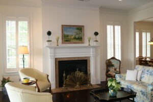 A living room with a white fireplace, armchairs, a patterned sofa, a brass fireplace screen, and a painting above the mantel.