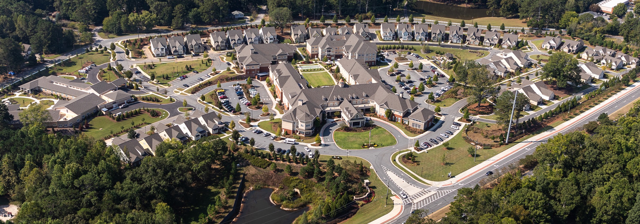 Aerial view of a large, modern residential complex with multiple buildings, landscaped gardens, curved roads, and surrounding trees.